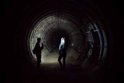 A man and a woman shining a light down an abandoned tunnel