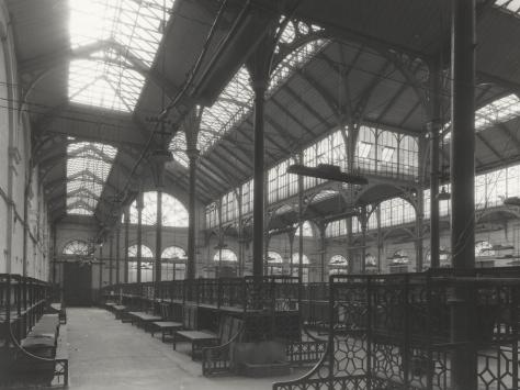 Black and white photo of an old building with high ceilings. metal framed windows ans market stalls